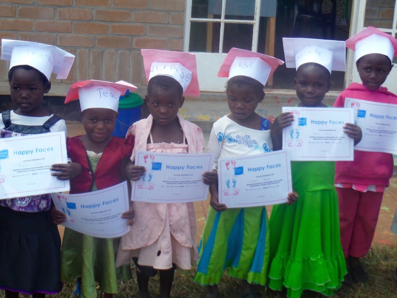 Graduating children with the profession they hope to work in written on their hats